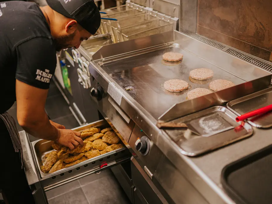 Medewerker bakt hamburger in restaurantkeuken