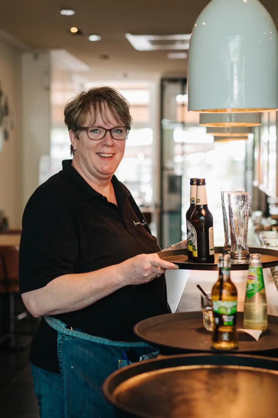 Horecamedewerkster met dienblad vol bier binnen in de zaak